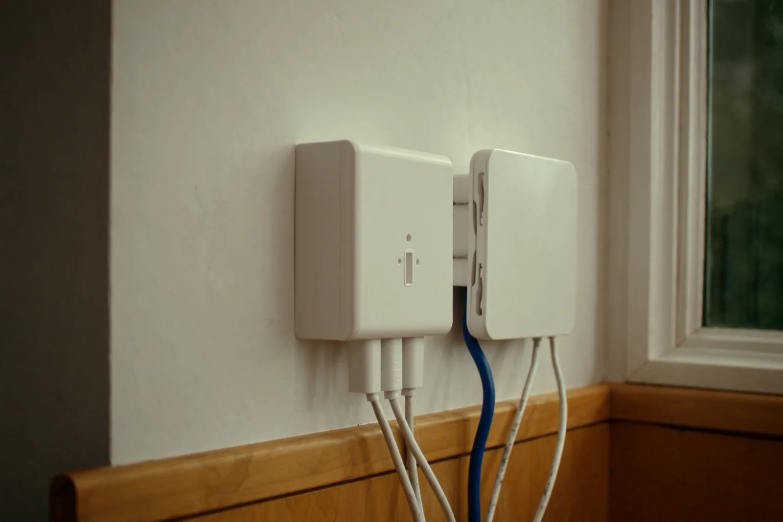 A white NBN connection box and a small router on an office wall, one blue cable between them
