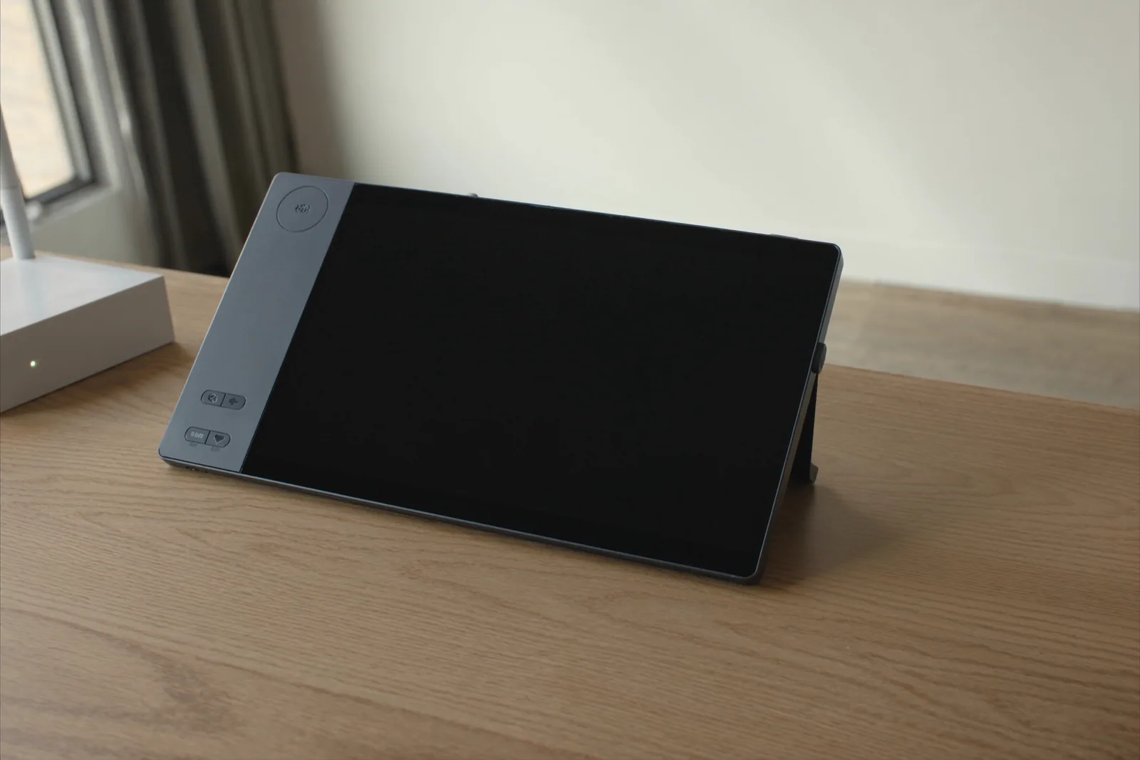A deskphone with a large dark screen beside a small white router on a timber desk